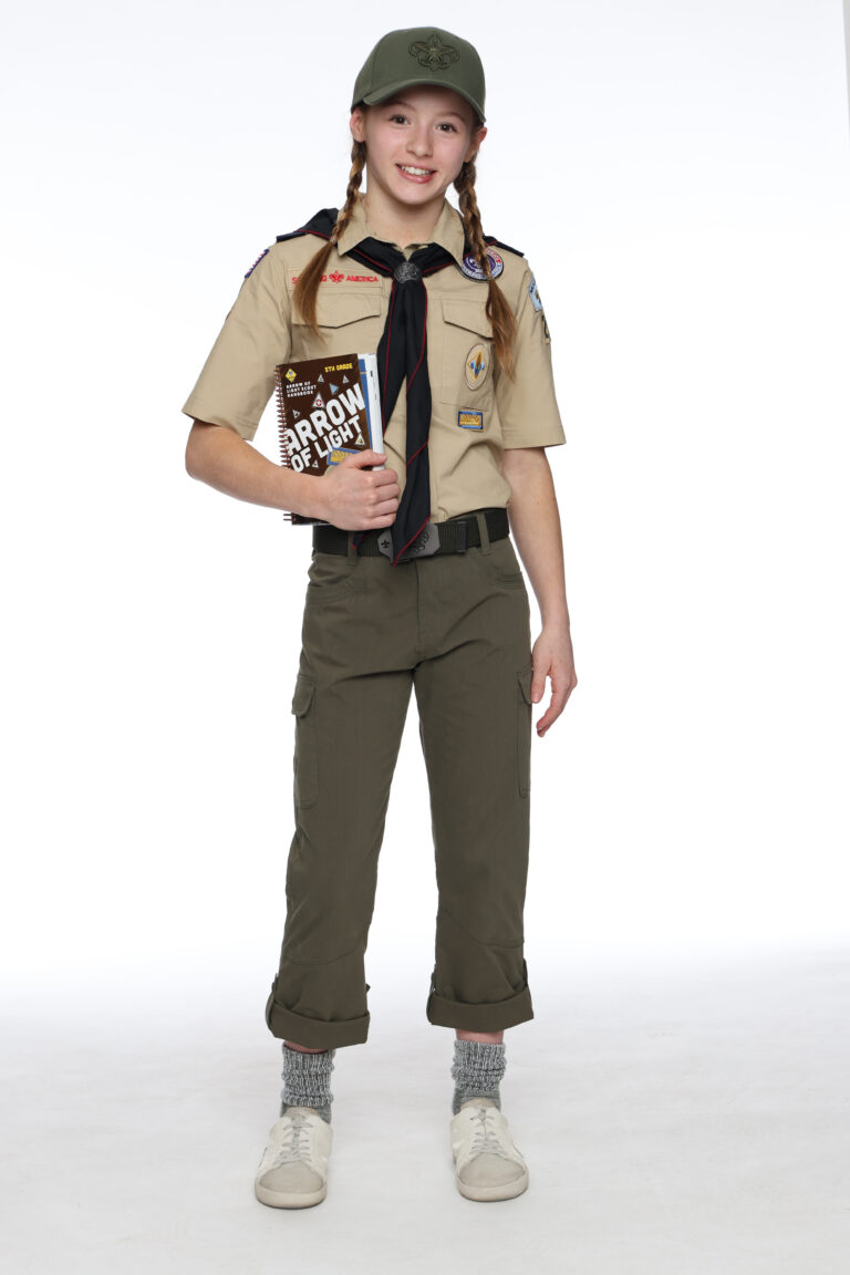 An Arrow of Light scout in tan uniform holding the Arrow of Light handbook