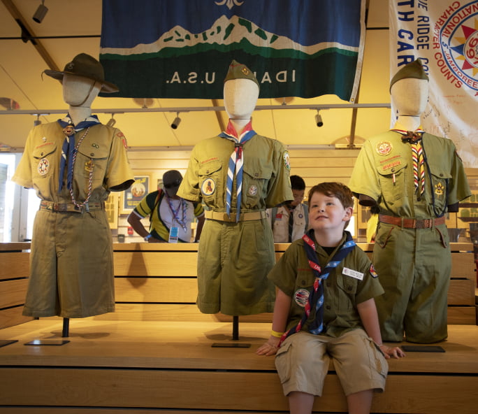 A scout sitting among mannequins displaying Scouting America uniforms