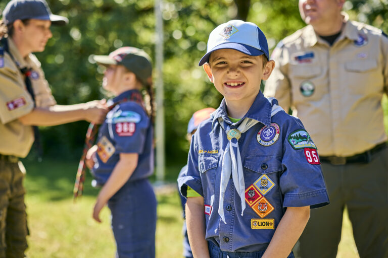 A smiling Cub Scout at an outdoor pack event, uniform covered in badges